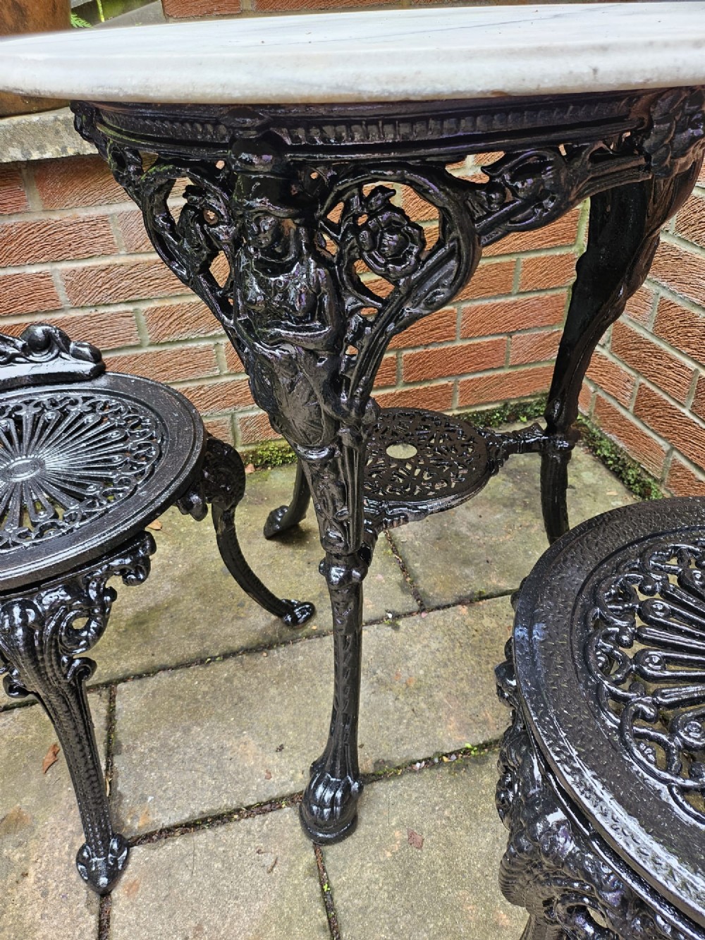 A circular white marble-topped table with a black cast-iron base alongside two matching black cast-iron chairs featuring ornate pierced scrollwork. View VII