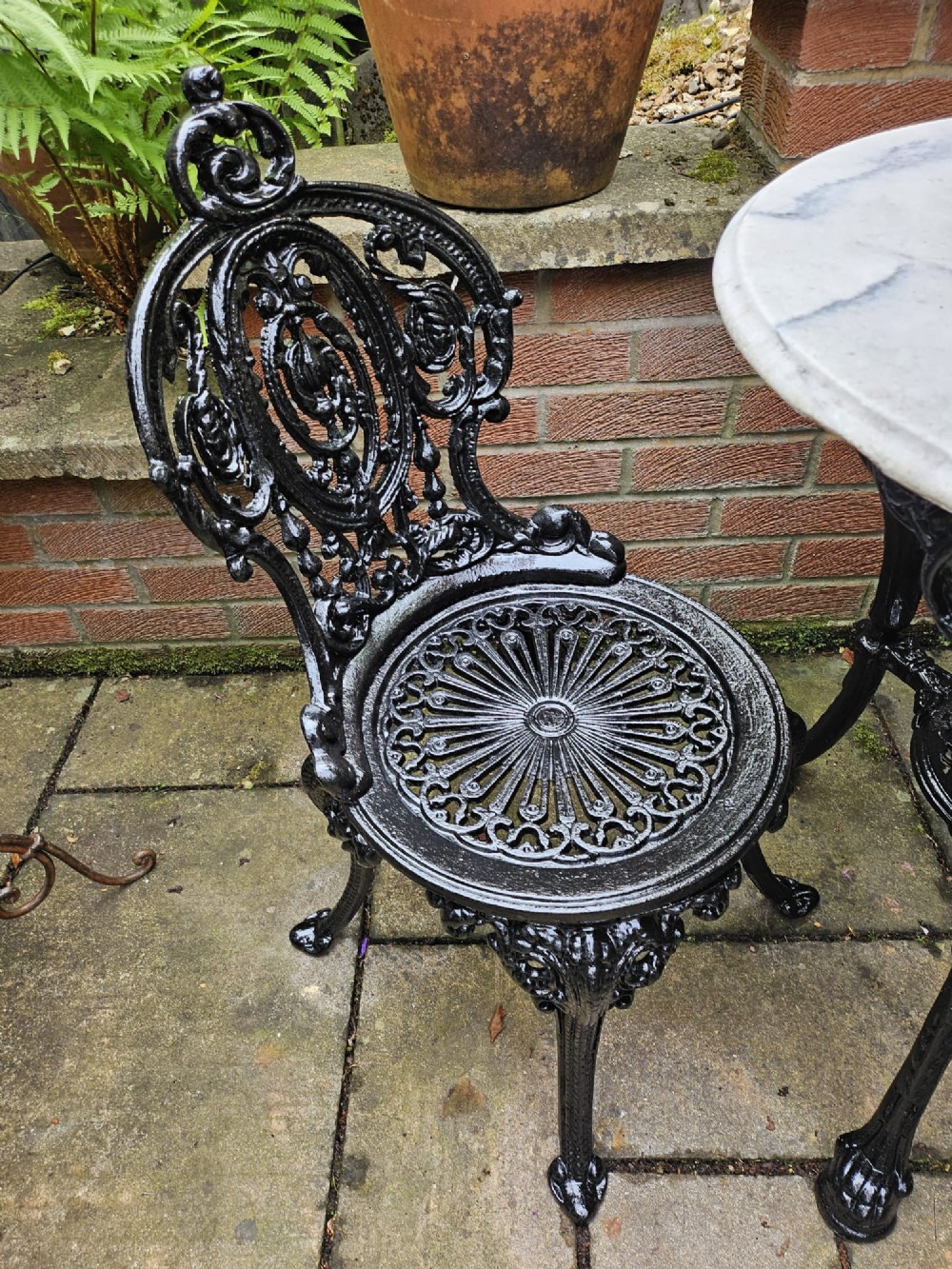A circular white marble-topped table with a black cast-iron base alongside two matching black cast-iron chairs featuring ornate pierced scrollwork. View VIII