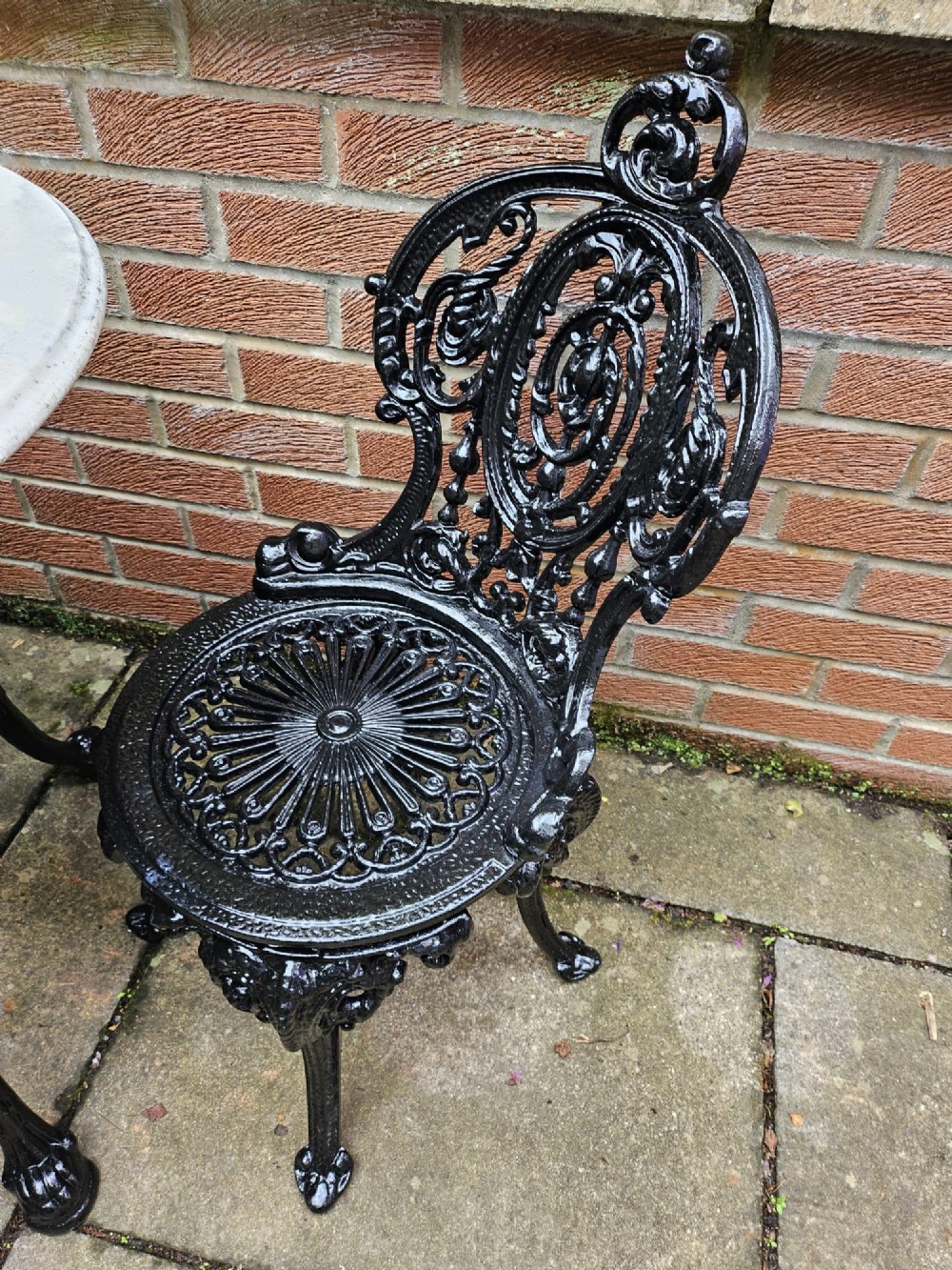 A circular white marble-topped table with a black cast-iron base alongside two matching black cast-iron chairs featuring ornate pierced scrollwork. View IX