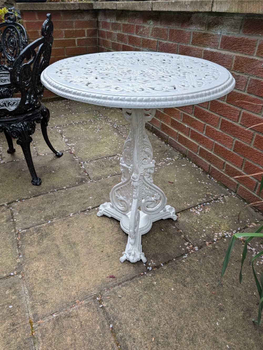 A white painted Victorian cast-iron garden bistro table featuring an intricately pierced circular top supported by an ornate tri-form pedestal base.