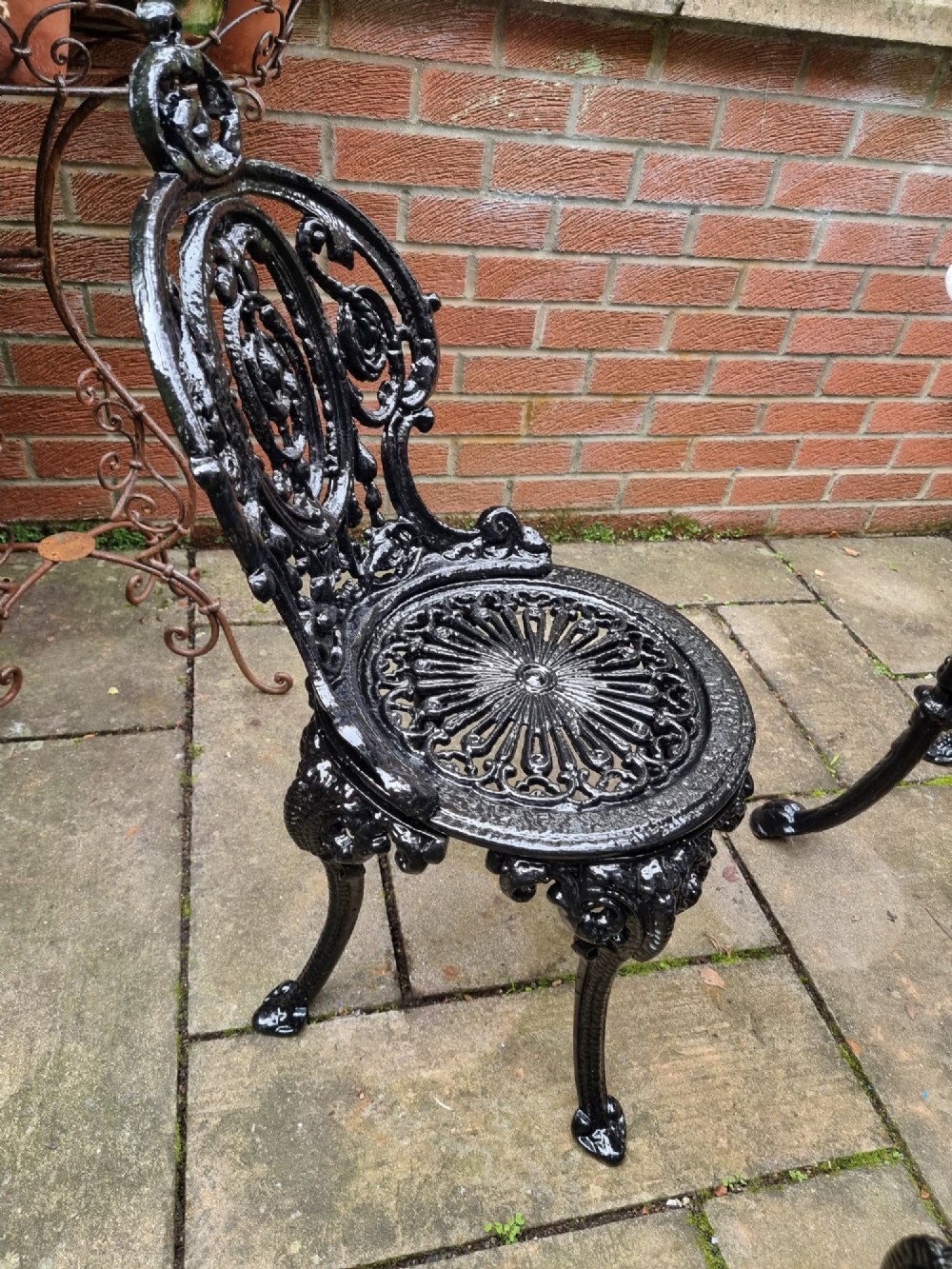 A five-piece garden set featuring a circular white marble-topped table and four black cast iron chairs with ornate pierced floral backrests. View IV