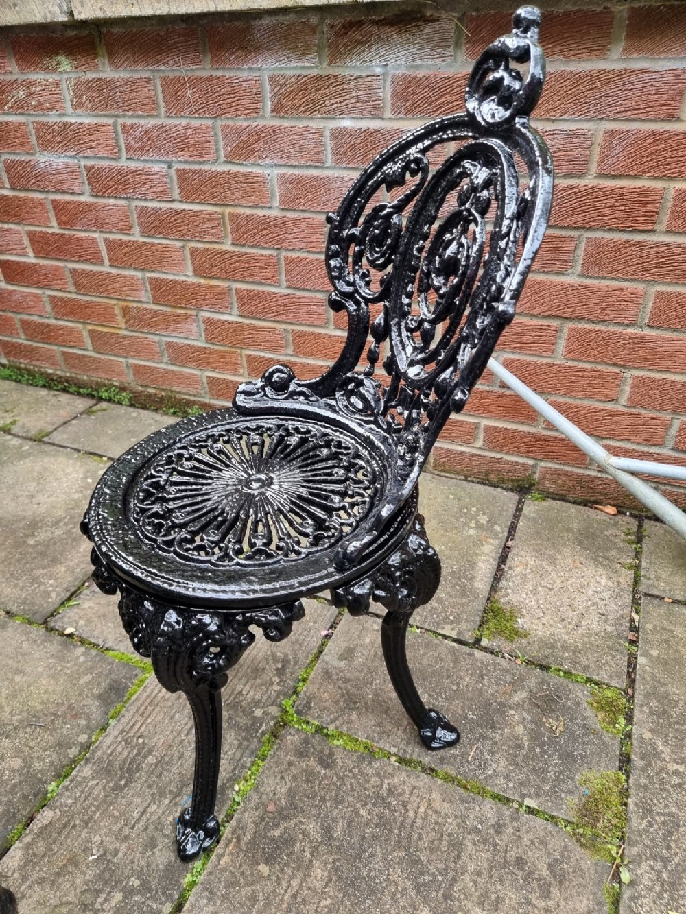 A five-piece garden set featuring a circular white marble-topped table and four black cast iron chairs with ornate pierced floral backrests. View VI