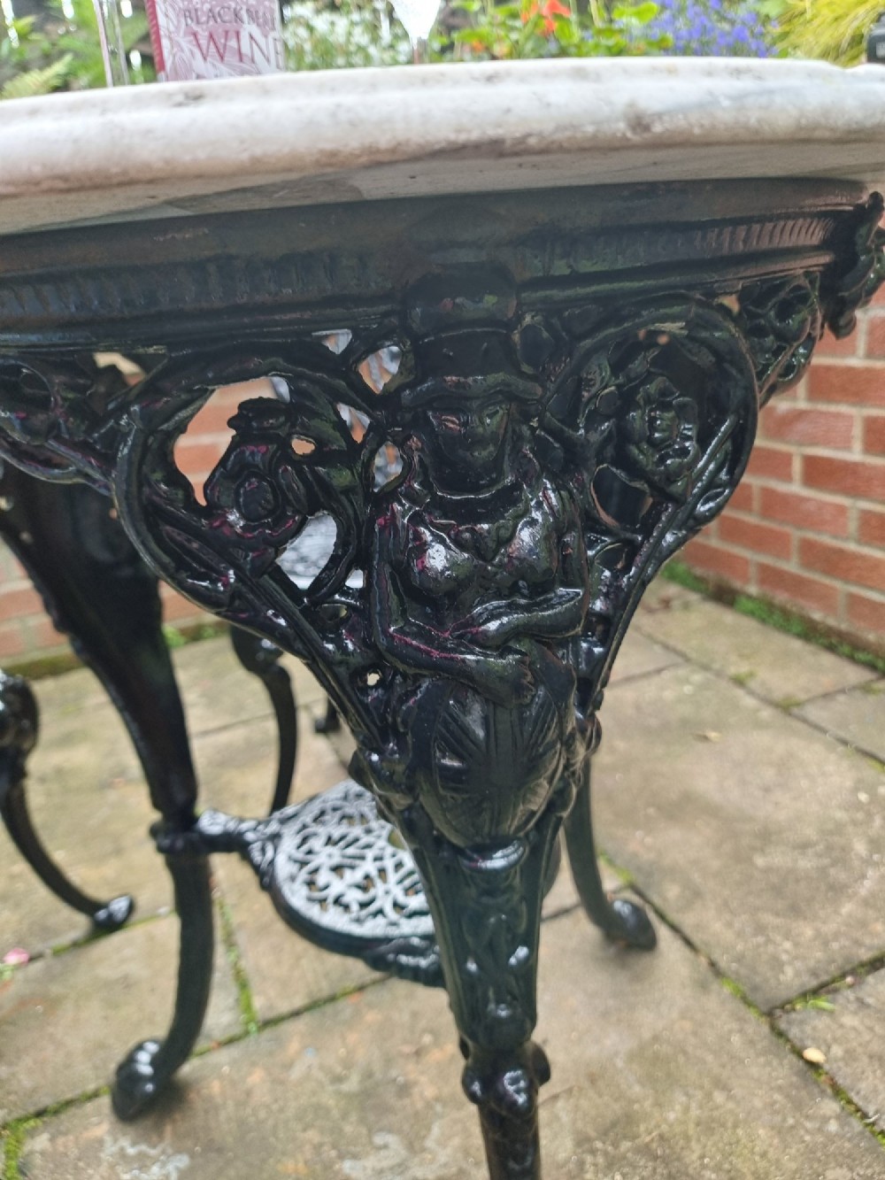 A five-piece garden set featuring a circular white marble-topped table and four black cast iron chairs with ornate pierced floral backrests. View VII