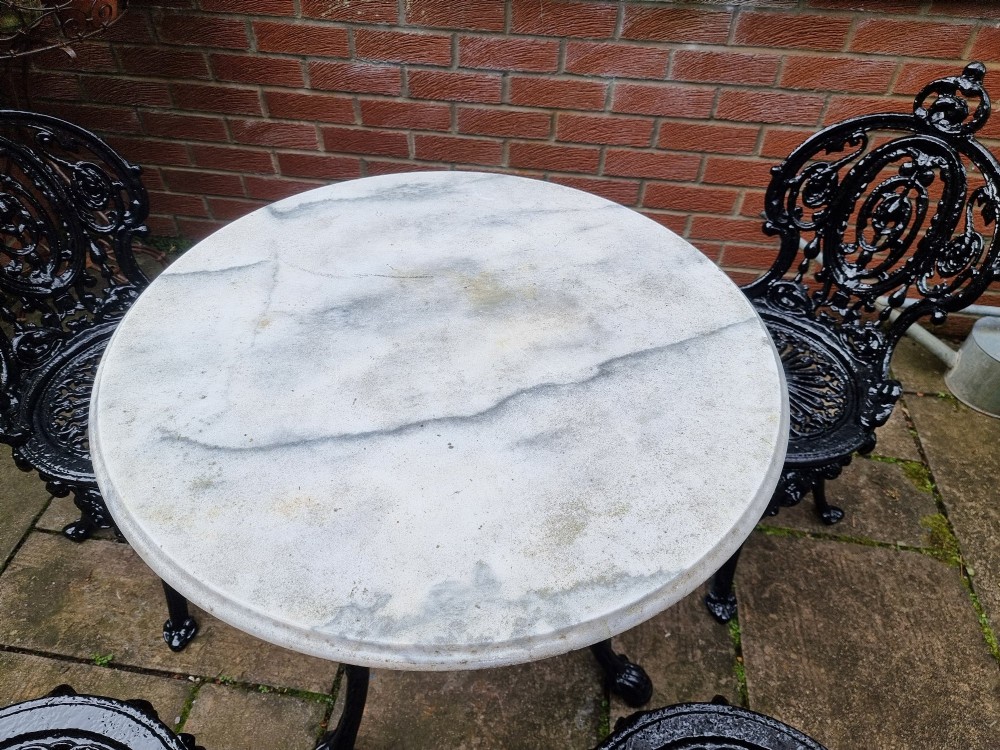A five-piece garden set featuring a circular white marble-topped table and four black cast iron chairs with ornate pierced floral backrests. View VIII