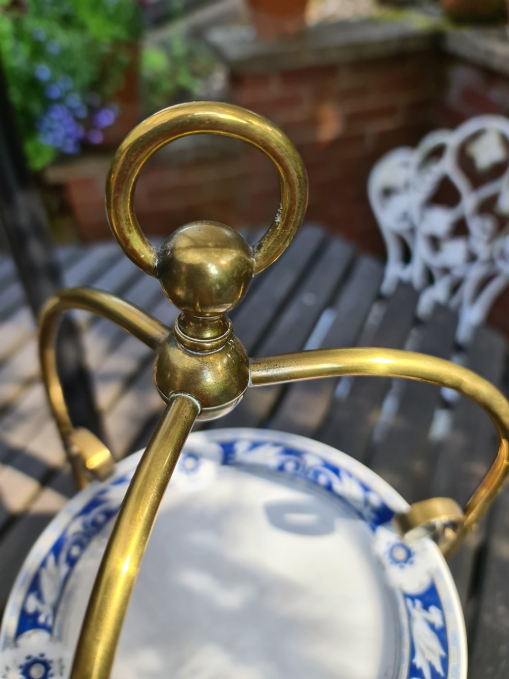 A three-tiered Edwardian cake stand featuring a brass metal frame with a top loop handle holding three blue and white ceramic plates. View II