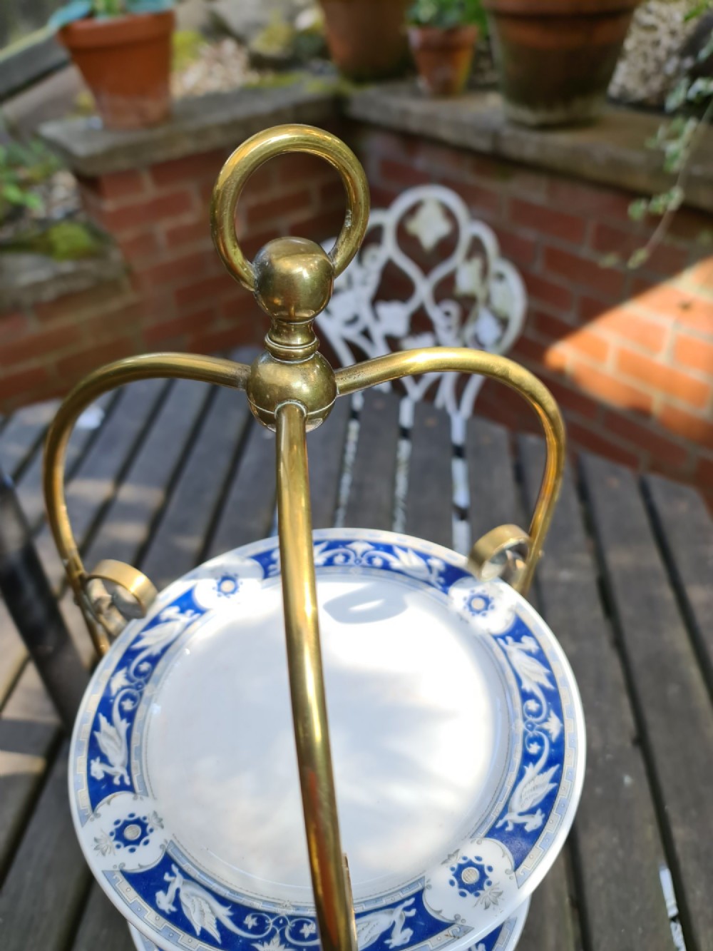 A three-tiered Edwardian cake stand featuring a brass metal frame with a top loop handle holding three blue and white ceramic plates. View III