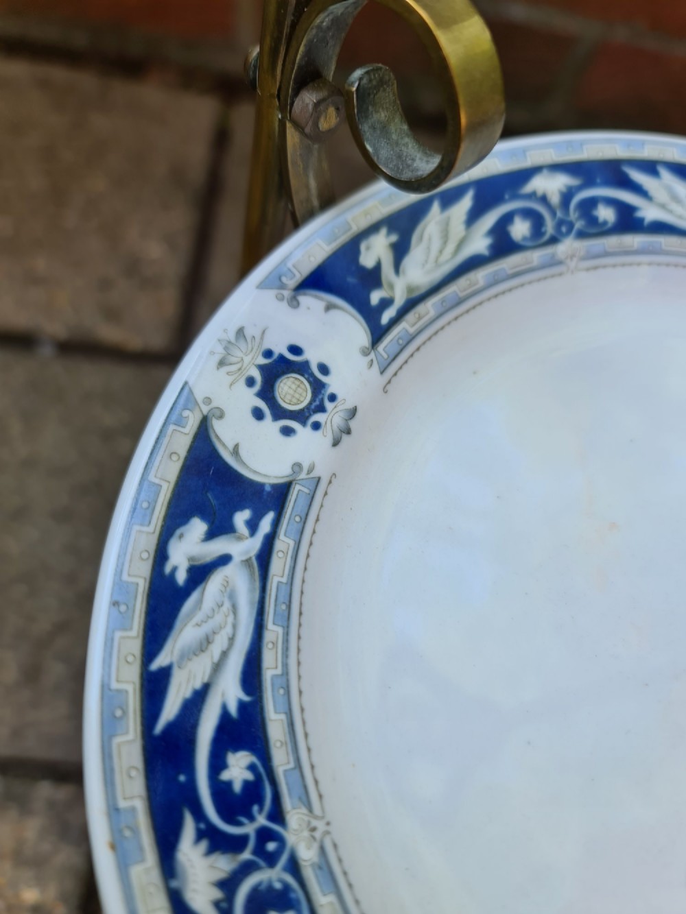 A three-tiered Edwardian cake stand featuring a brass metal frame with a top loop handle holding three blue and white ceramic plates. View IX