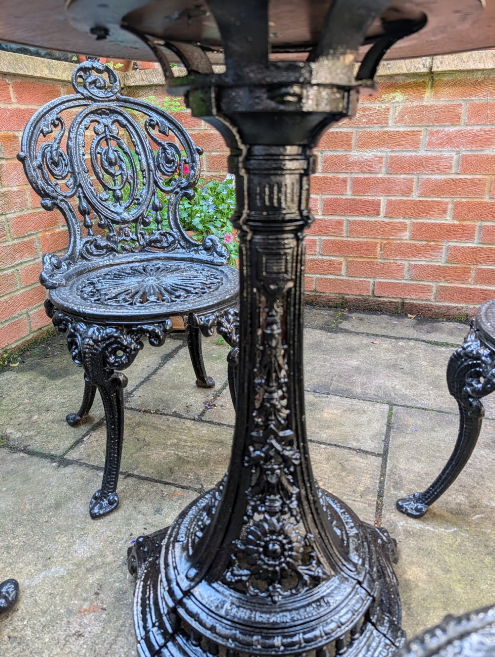 A Victorian cast-iron garden set featuring a circular copper-topped pedestal table surrounded by four ornate black cast-iron chairs with foliage-patterned backrests. View V