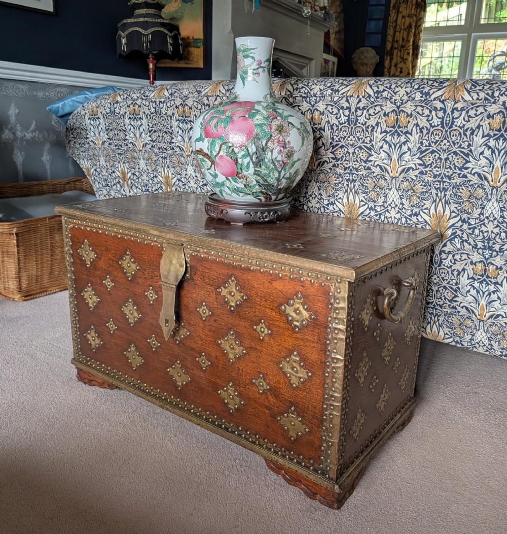 A rectangular padouk wood storage chest decorated with geometric brass mounts, brass studding, side carrying handles, and a central brass lock clasp. View II