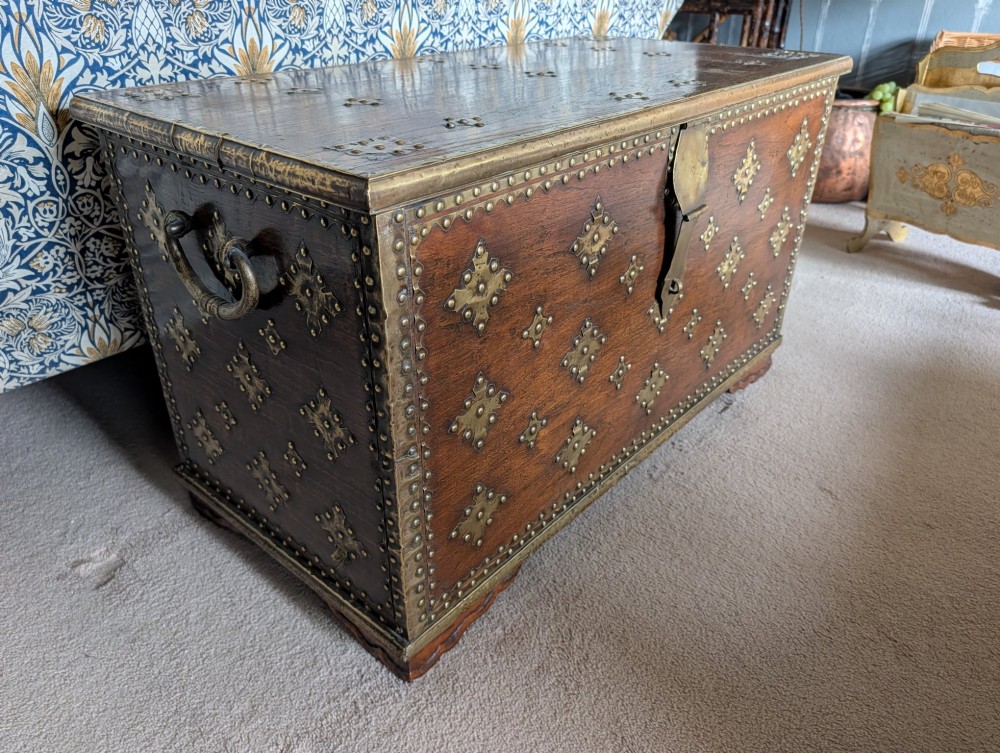 A rectangular padouk wood storage chest decorated with geometric brass mounts, brass studding, side carrying handles, and a central brass lock clasp. View III