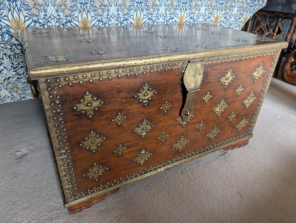 A rectangular padouk wood storage chest decorated with geometric brass mounts, brass studding, side carrying handles, and a central brass lock clasp. View IV