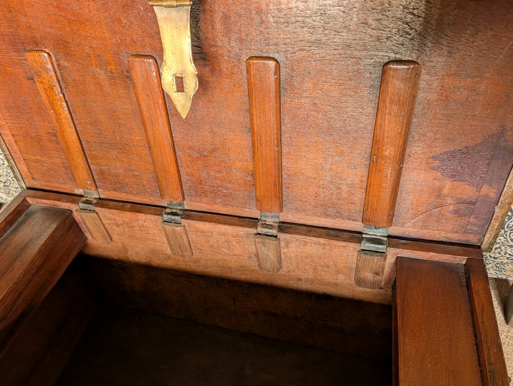 A rectangular padouk wood storage chest decorated with geometric brass mounts, brass studding, side carrying handles, and a central brass lock clasp. View VI