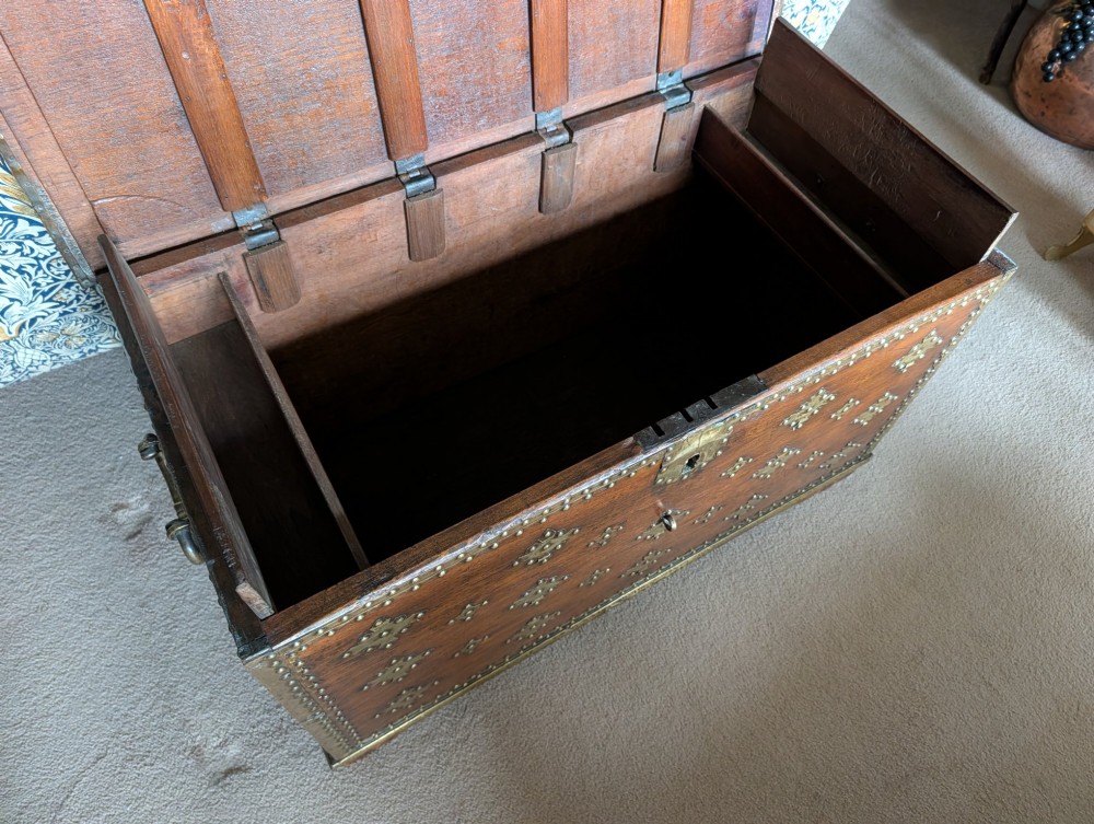 A rectangular padouk wood storage chest decorated with geometric brass mounts, brass studding, side carrying handles, and a central brass lock clasp. View VII
