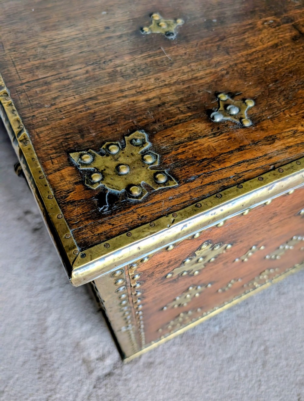 A rectangular padouk wood storage chest decorated with geometric brass mounts, brass studding, side carrying handles, and a central brass lock clasp. View VIII