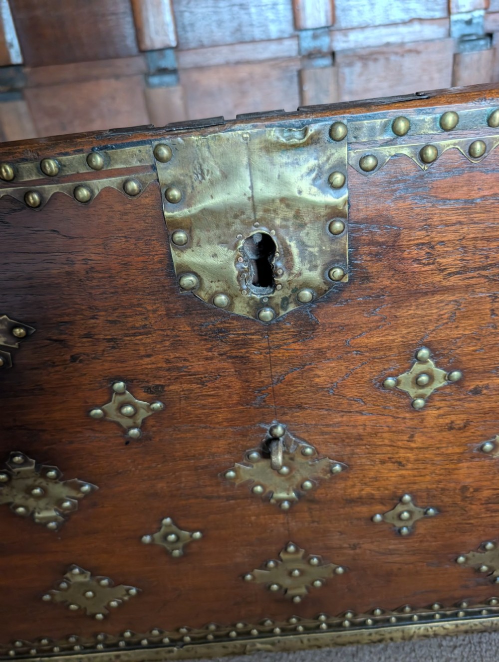A rectangular padouk wood storage chest decorated with geometric brass mounts, brass studding, side carrying handles, and a central brass lock clasp. View IX