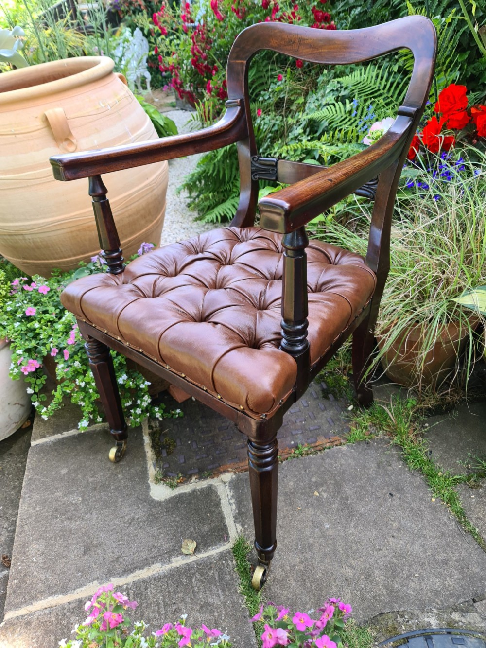 Early 19th-century mahogany desk chair featuring a curved back rail, turned front legs on brass castors, and a buttoned brown leather seat. View III