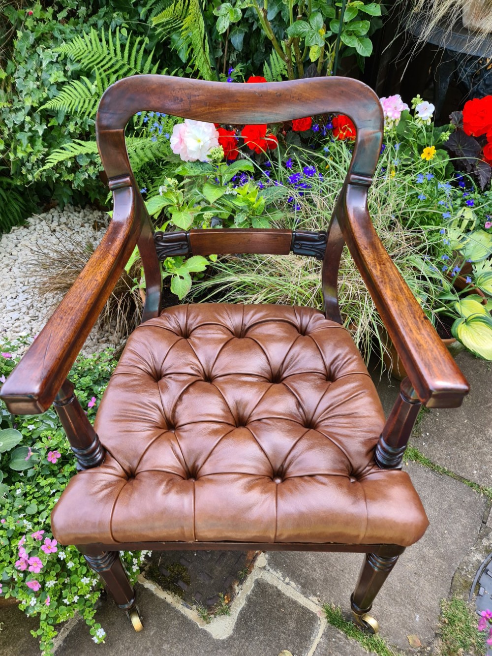 Early 19th-century mahogany desk chair featuring a curved back rail, turned front legs on brass castors, and a buttoned brown leather seat. View VII