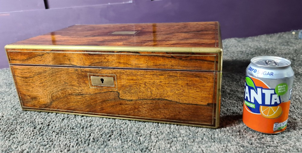 A rectangular rosewood box featuring brass edge binding, inlaid brass stringing, a brass escutcheon, and a tassel key inserted in the lock. View X