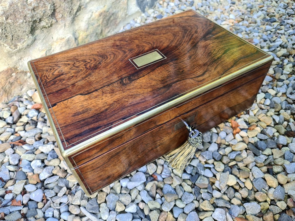 A rectangular rosewood box featuring brass edge binding, inlaid brass stringing, a brass escutcheon, and a tassel key inserted in the lock. View XI