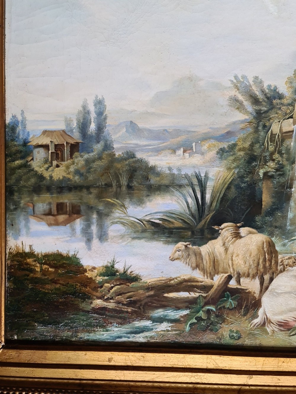 An oil painting depicting a Rococo pastoral scene with figures and sheep by a stream, set within a heavy gilded frame. View V