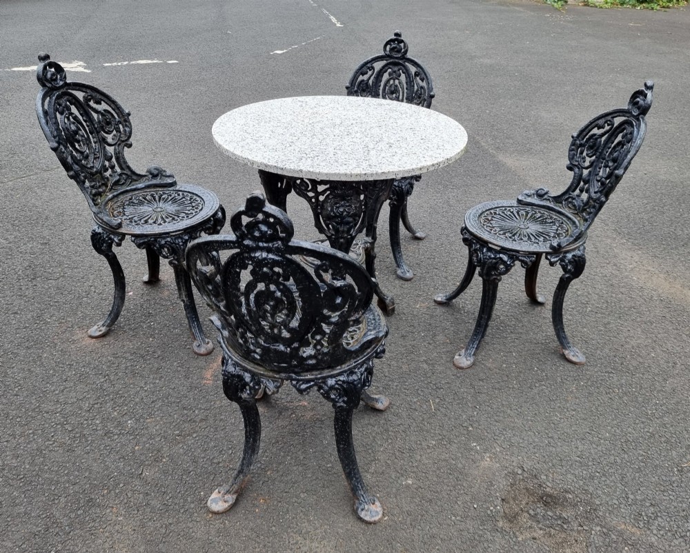 A black cast-iron outdoor bistro set featuring a circular stone-topped table and four matching ornate openwork chairs. View II