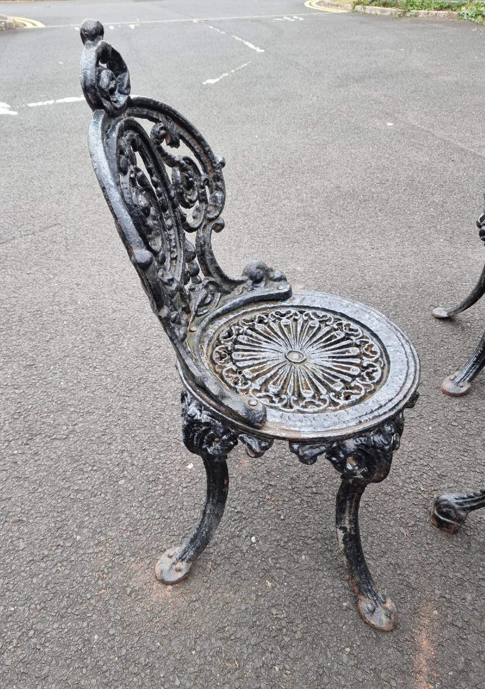 A black cast-iron outdoor bistro set featuring a circular stone-topped table and four matching ornate openwork chairs. View III