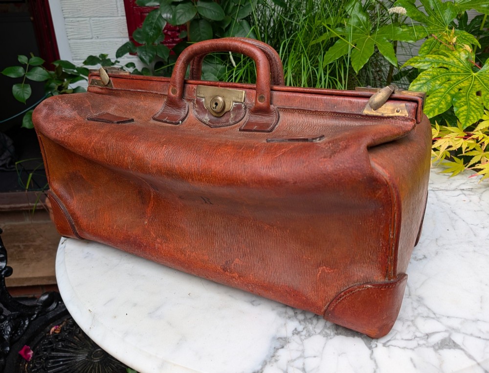 A Victorian brown leather Gladstone travel bag with a central brass lever lock and twin stitched handles. View II