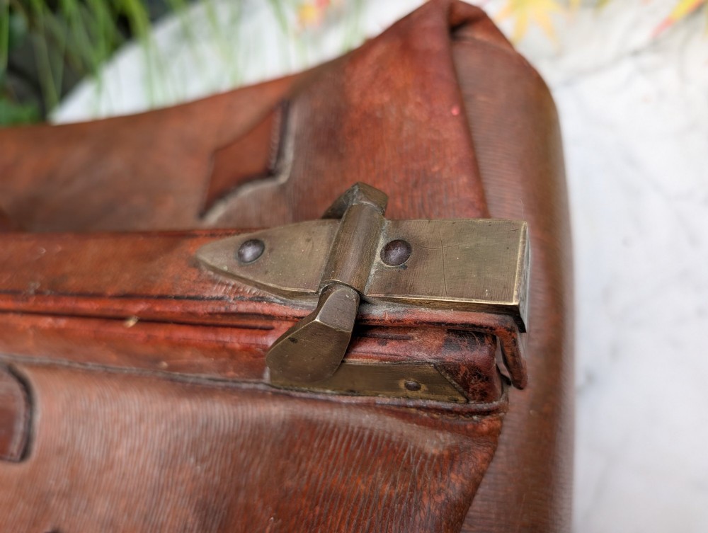 A Victorian brown leather Gladstone travel bag with a central brass lever lock and twin stitched handles. View V