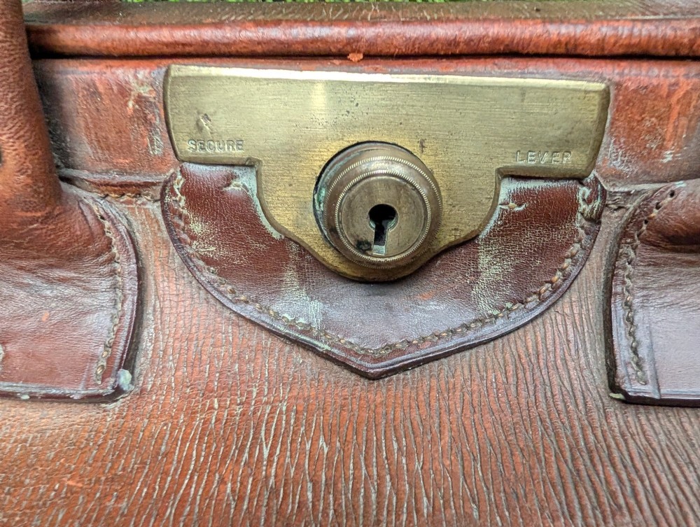 A Victorian brown leather Gladstone travel bag with a central brass lever lock and twin stitched handles. View VI