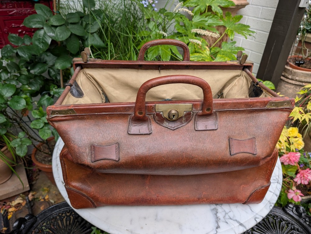 A Victorian brown leather Gladstone travel bag with a central brass lever lock and twin stitched handles. View X