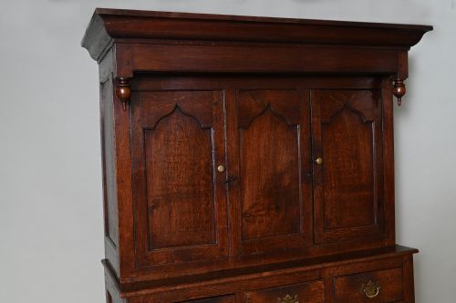 fig 1. An 18th-century dark oak Welsh press cupboard featuring upper ogee arched panel doors, turned drop finials, three middle drawers, and a double-door base.