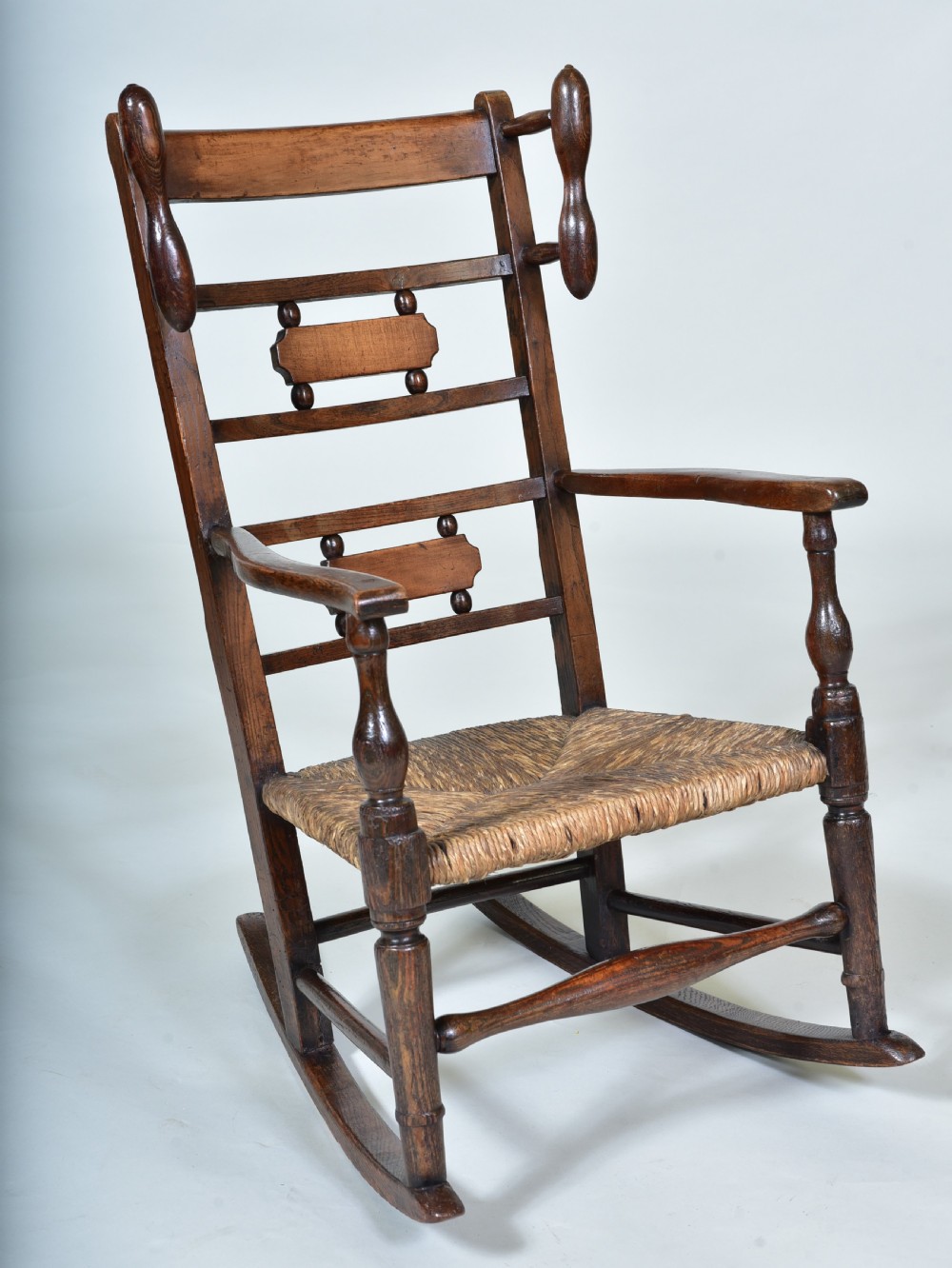 A 19th-century childs dark wood rocking chair featuring a ladder back structure, turned finials, shaped splats, and a woven rush seat.