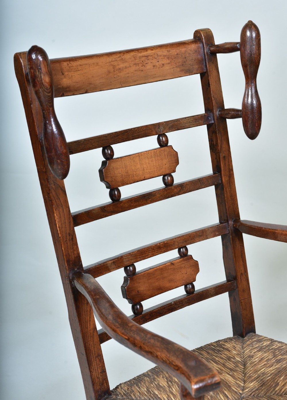A 19th-century childs dark wood rocking chair featuring a ladder back structure, turned finials, shaped splats, and a woven rush seat. View II