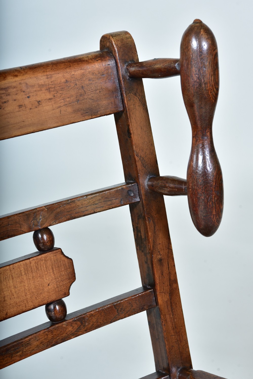 A 19th-century childs dark wood rocking chair featuring a ladder back structure, turned finials, shaped splats, and a woven rush seat. View III