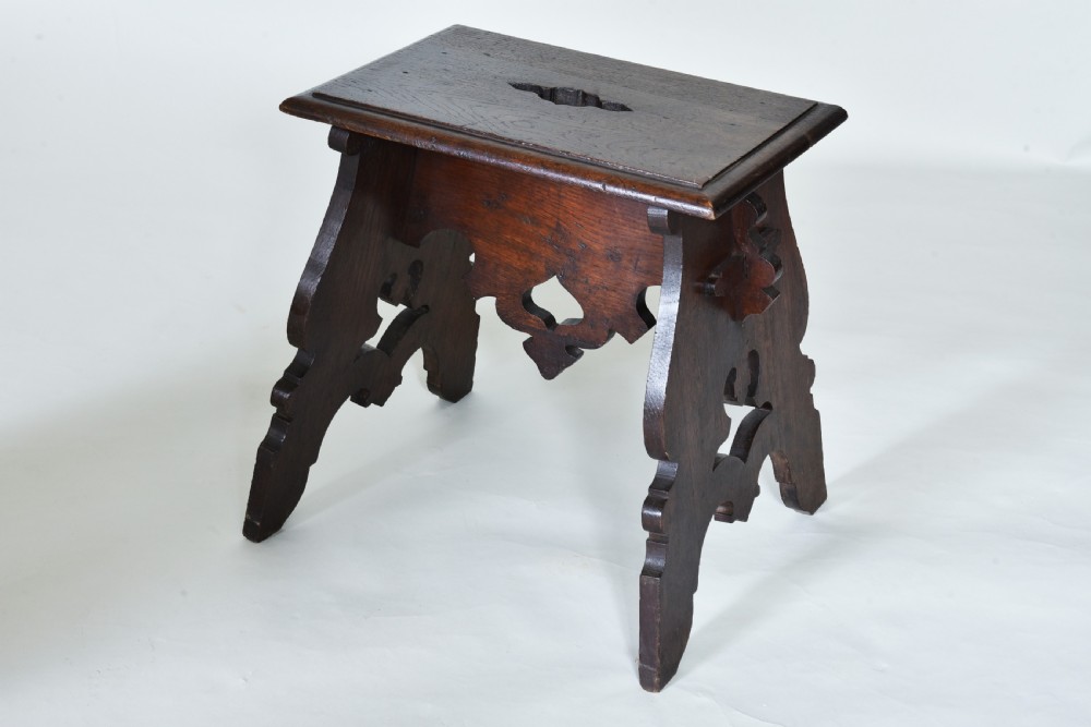 A small dark oak wooden stool featuring pierced fretwork sides, a cut-out carrying handle on the rectangular top, and shaped aprons.