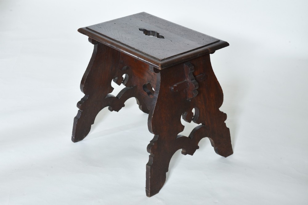 A small dark oak wooden stool featuring pierced fretwork sides, a cut-out carrying handle on the rectangular top, and shaped aprons. View II