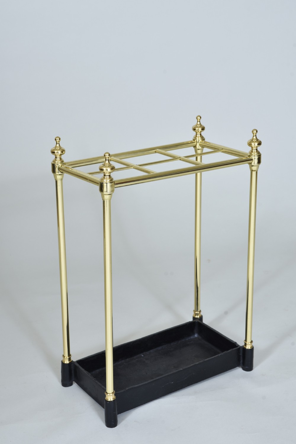 A Victorian brass umbrella stand featuring a six-compartment upper grid, turned finials, upright supports, and a black cast iron drip tray.