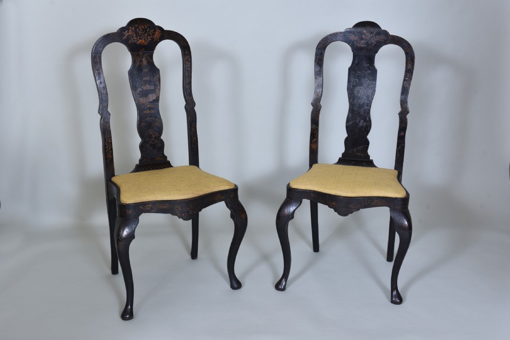 A pair of black lacquered Queen Anne style side chairs featuring vasiform splats, hand-painted gold Chinoiserie patterns, cabriole front legs, and yellow upholstered drop-in seats.