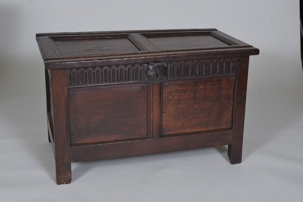 A dark oak 17th-century coffer featuring a carved fluted upper frieze, twin front panels, and a central iron lock plate. View II
