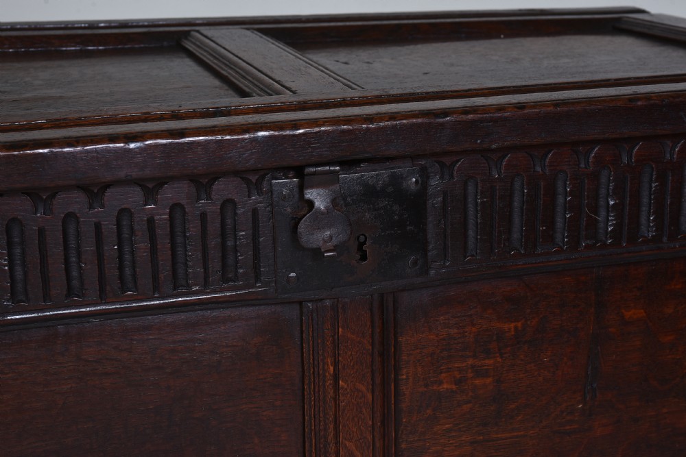 A dark oak 17th-century coffer featuring a carved fluted upper frieze, twin front panels, and a central iron lock plate. View VII