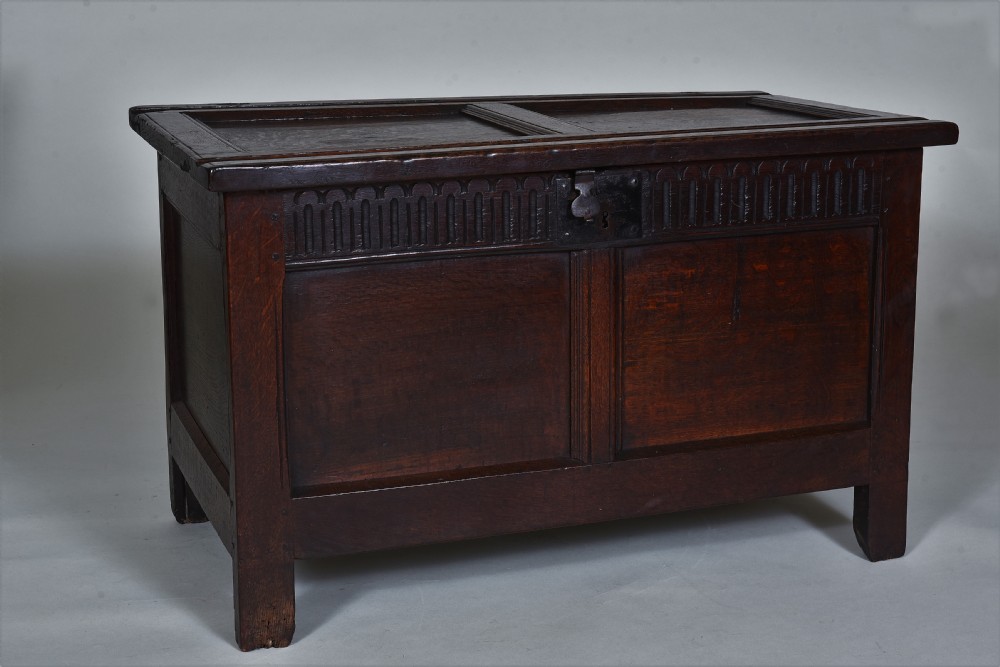 A dark oak 17th-century coffer featuring a carved fluted upper frieze, twin front panels, and a central iron lock plate.