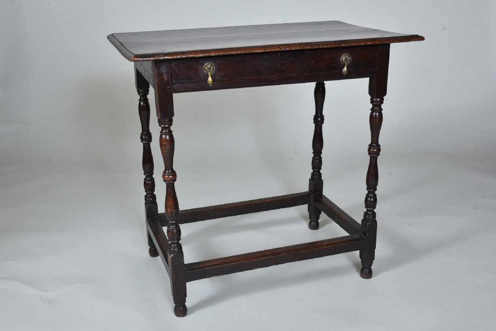 A 17th century dark oak side table featuring a single drawer with brass drop handles, turned legs, and a low box stretcher. View II
