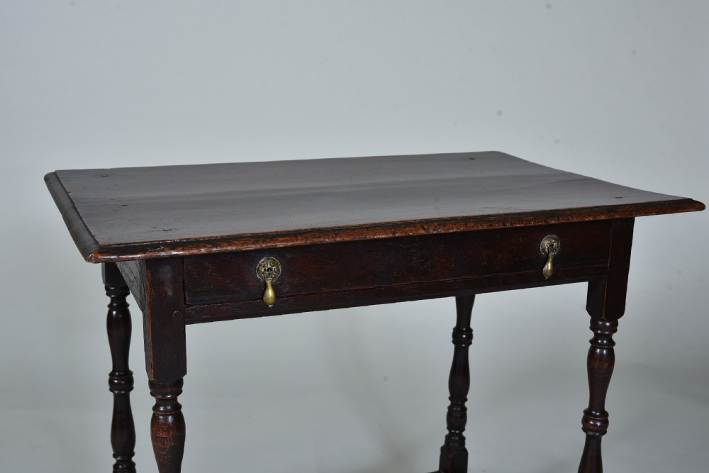 A 17th century dark oak side table featuring a single drawer with brass drop handles, turned legs, and a low box stretcher. View III