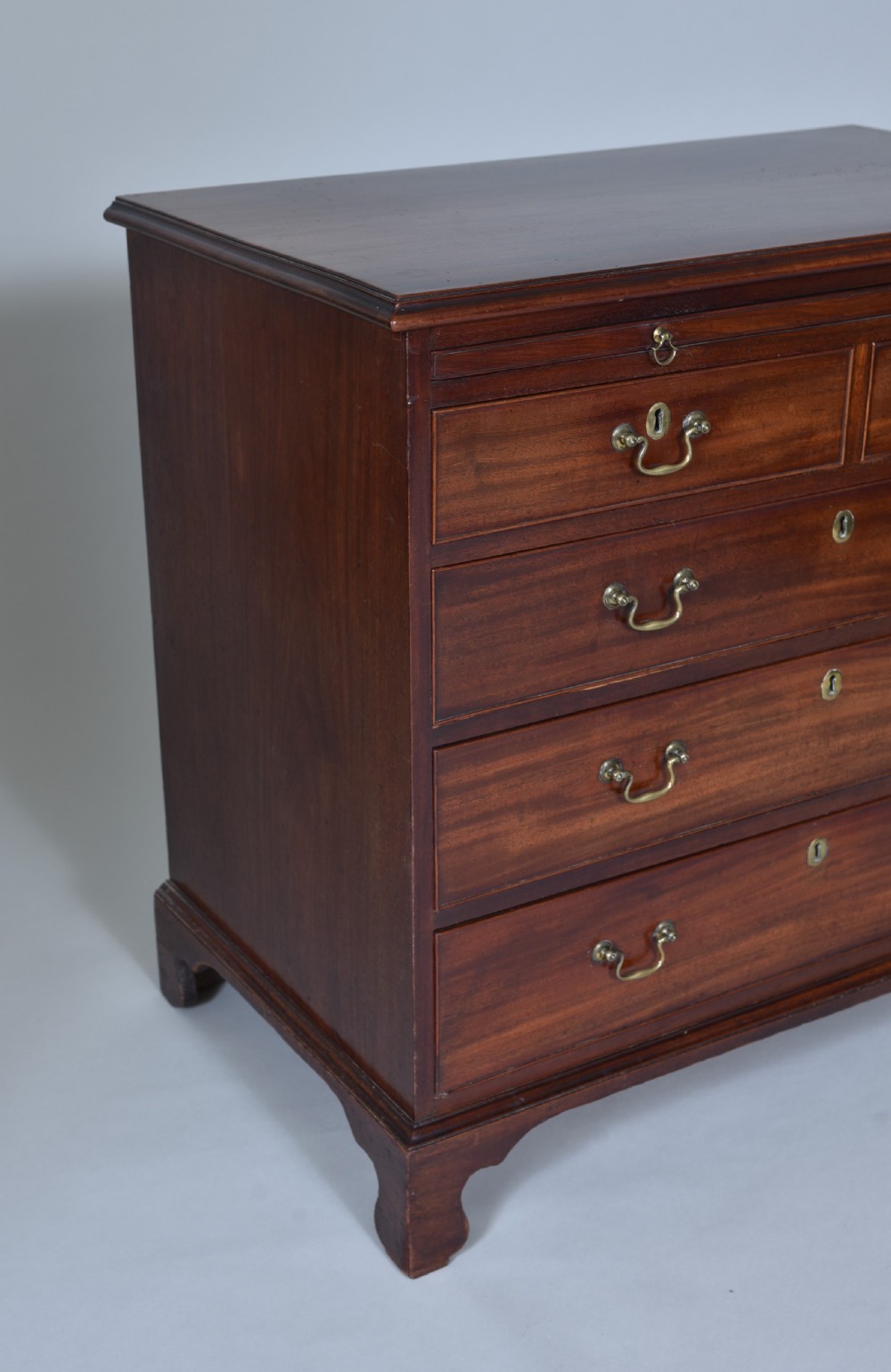 A Georgian mahogany chest of drawers featuring a pull-out brushing slide, two short drawers over three long graduated drawers, brass drop handles, and bracket feet. View IV