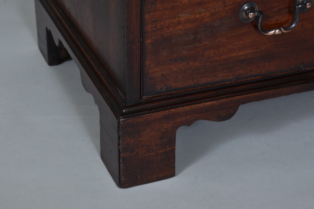 A Georgian mahogany chest of drawers featuring four graduated long drawers with brass swan-neck handles, a pull-out brushing slide, and bracket feet. View V