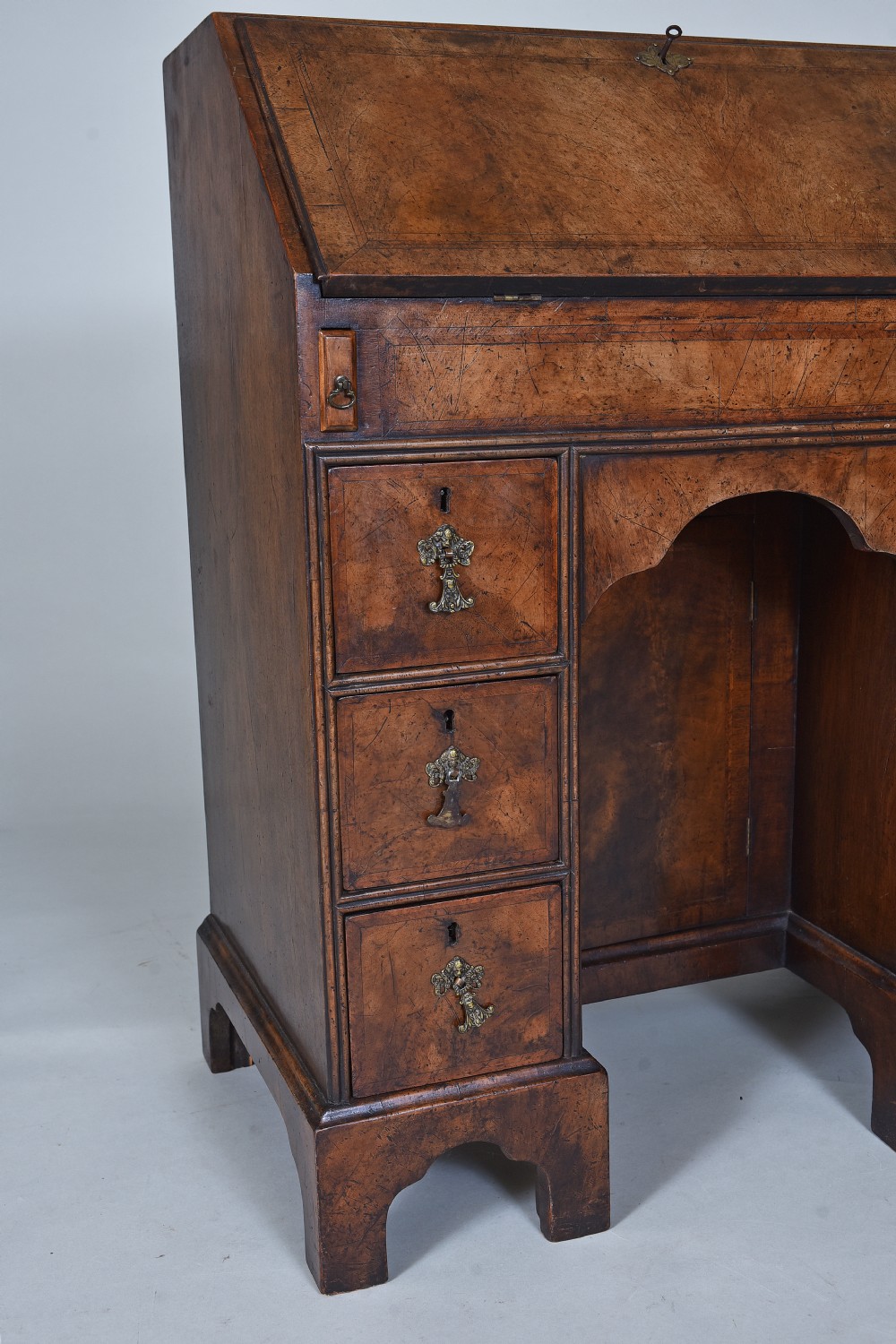 An antique burr walnut kneehole bureau featuring a slant-front writing slope, brass drop handles, and bracket feet. View II