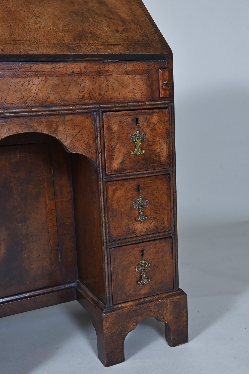 An antique burr walnut kneehole bureau featuring a slant-front writing slope, brass drop handles, and bracket feet. View III
