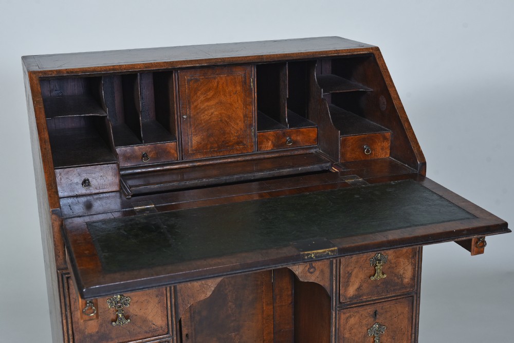 An antique burr walnut kneehole bureau featuring a slant-front writing slope, brass drop handles, and bracket feet. View V