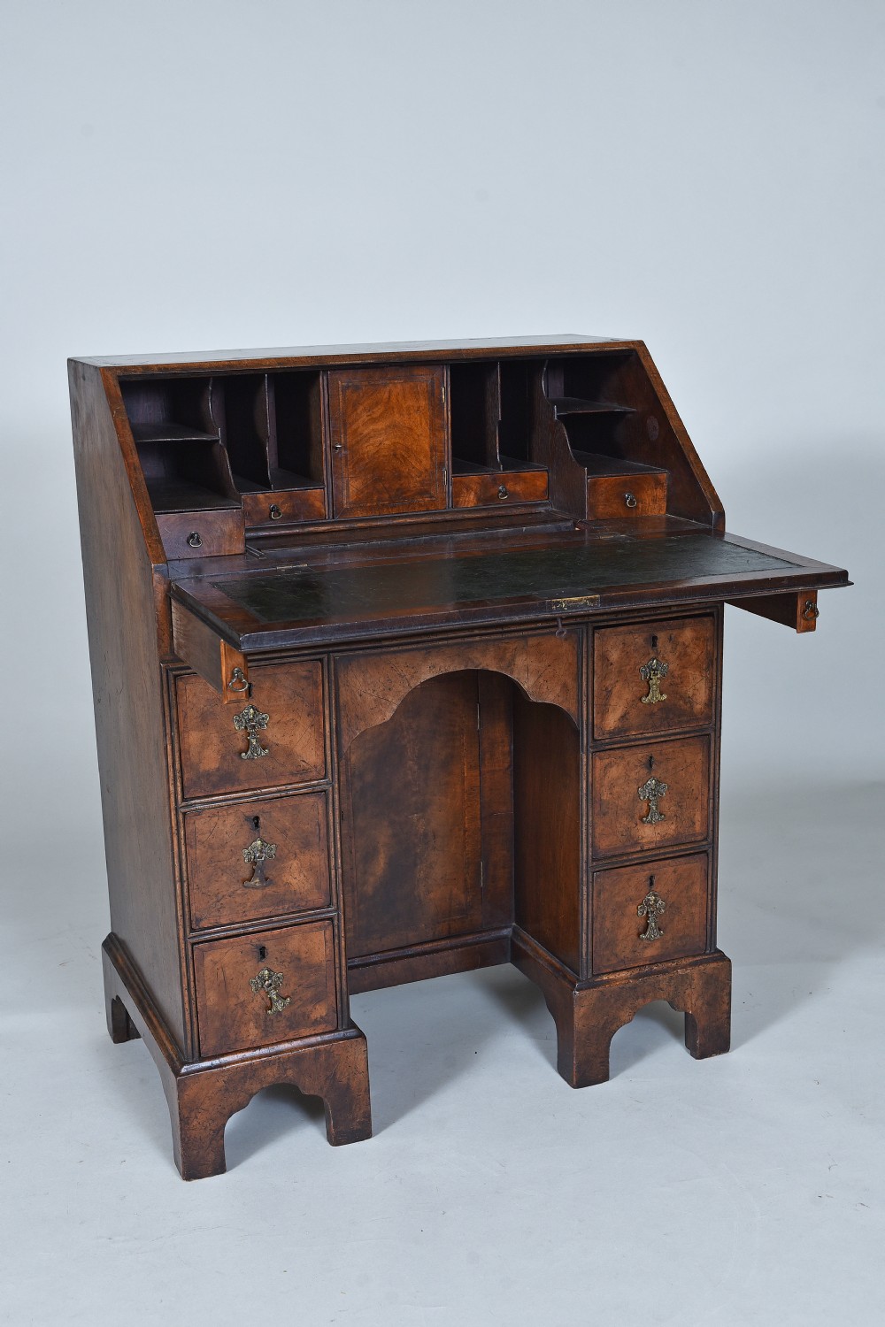An antique burr walnut kneehole bureau featuring a slant-front writing slope, brass drop handles, and bracket feet. View VI