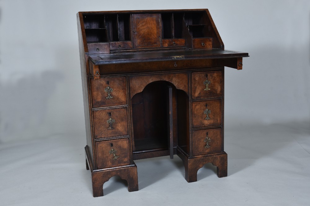 An antique burr walnut kneehole bureau featuring a slant-front writing slope, brass drop handles, and bracket feet. View VII